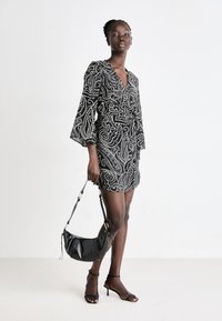 Minidress paisley bianco e nero con maniche a campana e dettaglio anteriore con nodo. Abbinato a una borsa nera e sandali con tacco sottile.