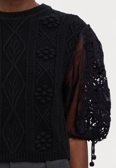 Černý pletený top s texturou a květinovými vzory na přední straně, se síťovanými balónovými rukávy, ribbovaným výstřihem a akcenty se stahovací šňůrkou.