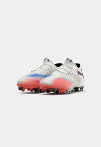 Cleats feature a white base with red and blue gradient detailing, textured pattern, and black studs. Design includes a sleek, aerodynamic shape.