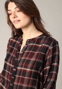 Chemise à carreaux boutonnée en bordeaux, noir et crème. Présente un col arrondi, des manches longues et une coupe décontractée avec un tissu texturé.