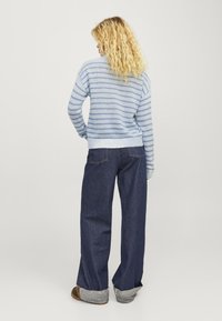Világoskék és fehér csíkos kötött pulóver, laza szabással, sötétkék széles lábú farmerral párosítva, amelynek felgöngyölt ujja és látható varrásai vannak.
