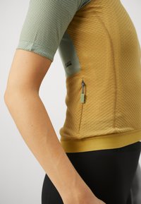 Sportliches Kurzarmshirt aus strukturiertem, honigwabenförmigem Stoff in Hellgrün und goldgelb, mit einer seitlichen Zipper-Tasche.
