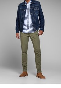 Veste en denim bleu foncé, chemise rayée blanche et bleue, pantalon vert olive et bottines beige. Caractéristiques : poche poitrine et design ajusté.