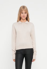 Pull en maille beige avec col polo, patte de boutonnage à quatre boutons et manches longues. Texture douce avec ourlet et poignets côtelés.