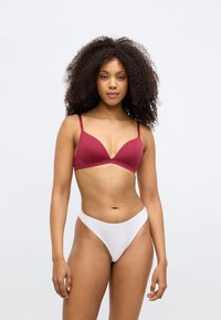 Μπουρντό σουτιέν χωρίς μπανέλες με τριγωνικά cups και λεπτές τιράντες, συνδυασμένο με ένα λευκό κλασικό thong. Λείο ύφασμα με μινιμαλιστικό σχέδιο.