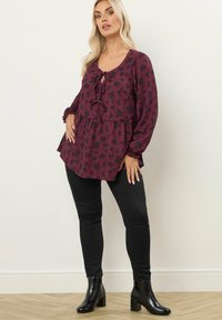 Blusa floreale bordeaux con scollatura a barchetta, maniche a balza e dettaglio con fiocco, abbinata a pantaloni neri aderenti e stivali neri alla caviglia.