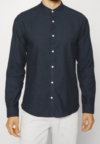 Camicia blu navy con colletto alla cinese, caratterizzata da un motivo testurizzato, maniche lunghe e bottoni bianchi per la chiusura.