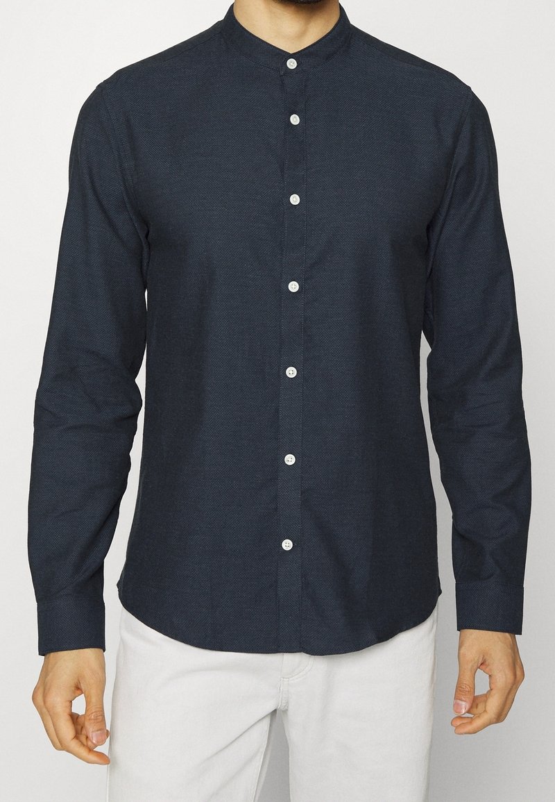 Camicia blu navy con colletto alla cinese, caratterizzata da un motivo testurizzato, maniche lunghe e bottoni bianchi per la chiusura.