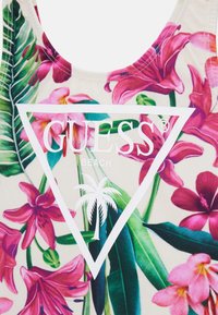 Badebeklædning med blomsterdesign, der har pink orkideer og grønne blade, samt et hvidt trekantet logo med teksten "GUESS BEACH" og et palmetræ.