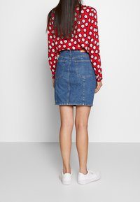 Jeanskjol i blått med en figursydd design, i midjehöjd med två bakfickor. Kombinerad med en röd mönstrad topp och vita sneakers.