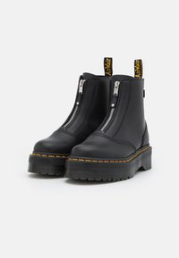 Black leather ankle boots with side zippers, yellow stitching accents, and a thick textured sole, featuring a pull tab on the back.