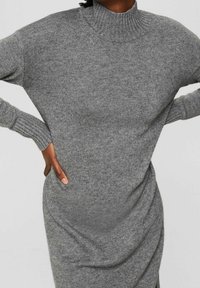 Robe en maille grise avec un col haut et des manches longues. Elle présente des détails côtelés et des poches latérales pour une fonctionnalité accrue.