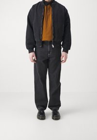 Czarna kurtka bomberka, pomarańczowa koszulka polo, czarne szerokie jeansy oraz czarne buty. Prosty design z zamkiem błyskawicznym i ściągaczami na kurtce.