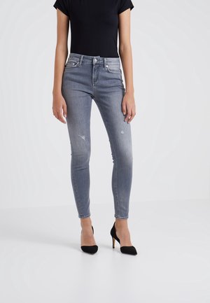 Jeans skinny de denim azul claro con detalles desgastados, diseño de talle alto y estilo de cinco bolsillos, combinados con tacones de aguja negros.