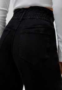 Svarta högmidjade byxor med en rynkad elastisk midja, med två bakfickor och en slät, texturerad tygfinish.