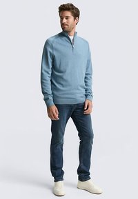 Pulover albastru deschis, cu textură, cu fermoar până la un sfert și manșete striate, asortat cu blugi din denim închis și adidași albi.