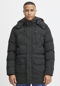 Abrigo parka acolchado de color verde oscuro con un cuello alto, capucha ajustable, bolsillos frontales y detalles de botones. Textura de tela suave.