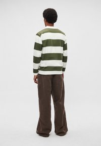 Rohelise ja valge triibulise kaelusega pika varrukaga särk, pruunide laia säärega pükstega, kujutatud tagantpoolt neutraalsel taustal.