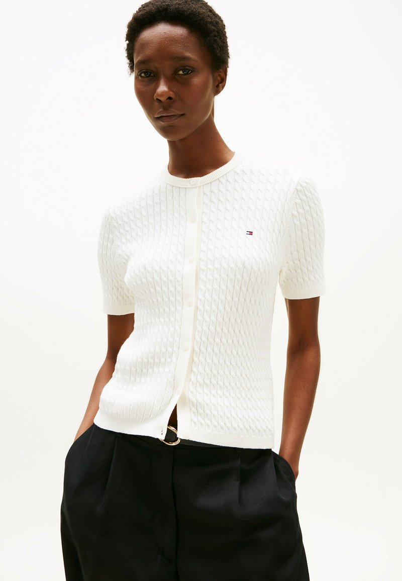 Biały, prążkowany kardigan z krótkim rękawem i zapięciem na guziki. Oferuje małe logo na lewej piersi oraz smukły krój.