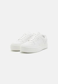 Hvide sneakers med en glat syntetisk overdel, flade snørebånd, perforeret tåboks og en tyk hvid gummisål. Minimalistisk design og rene linjer.