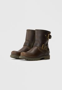Botas de cano curto em pele castanha com biqueira arredondada, detalhes em fivela e sola de borracha texturizada. Apresentam um fecho de correr para facilitar o calçar.