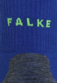 Calze blu e grigie con texture a coste e tallone imbottito. Presenta la scritta "FALKE" verde sulla sezione blu.