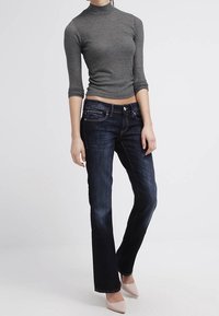 Maglia a collo alto grigia a coste con maniche a tre quarti abbinata a jeans scuri a zampa e tacchi color nude. Tessuto liscio, design aderente.