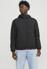 Black puffer jacket with a hood, zip closure, and side pockets; features a matte texture and a logo on the front left.