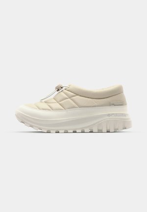 Béžové prošívané slip-on tenisky s tlustou bílou podrážkou, vybavené poutkem a elastickým stahováním pro nastavitelný fit, strukturovaný vzorek podrážky.