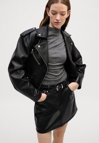 Crna kožna moto jakna sa srebrnim detaljima, džepovima na patentni zatvarač, nošena preko sivoj rolki. Uparen s crnom kožnom mini suknjom.