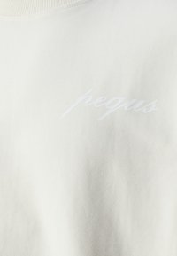 Vit bomullströja med en mjuk textur och en subtil broderad logotyp "pegus" i matchande tråd på bröstet.