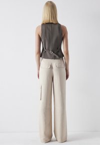 Szary bezrękawnik o dopasowanym kroju z zapięciem z tyłu, połączony z luźnymi beżowymi spodniami w szerokim kroju z bocznymi kieszeniami.