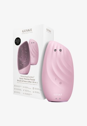 Brosse faciale thermo-sonique rose portable avec surface texturée et nœuds métalliques, avec sa boîte d’emballage blanche contenant les détails du produit.