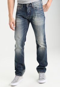 Denimjeans i blekblått med rak benpassform, femficksdesign och subtila slitningar vid låren. Kombineras med ljusgrå sneakers.