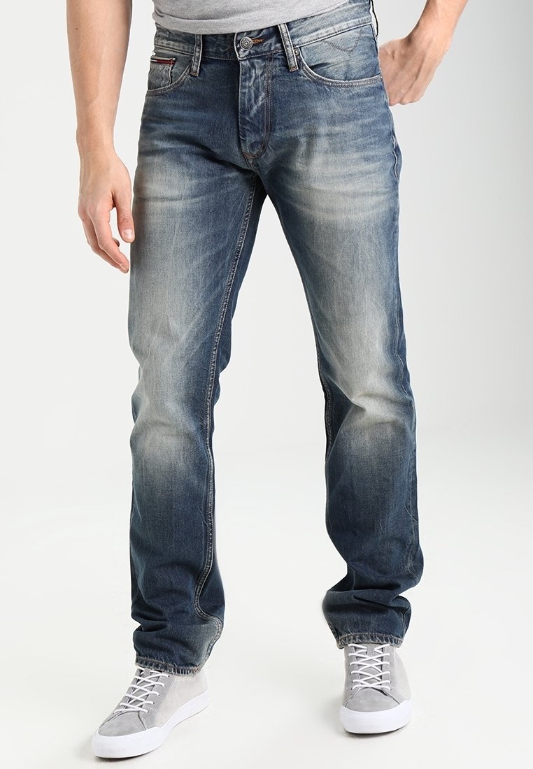 Denimjeans i blekblått med rak benpassform, femficksdesign och subtila slitningar vid låren. Kombineras med ljusgrå sneakers.