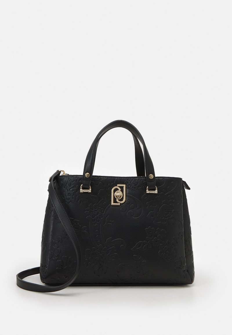 Sac à main noir texturé avec doubles poignées, une longue bandoulière et un détail de fermoir doré sur fond blanc uni.