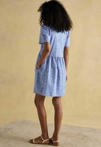 Lühikeste varrukatega sinine kleit, millel on lillemuster, rinna alt kokku kogutud talje ja taskud, valmistatud kerge materjali, kokku sobitatud beežide sandaalidega.