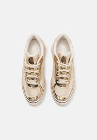 Sneaker atletiche dorate con una tomaia in rete testurizzata, dettagli metallici, lacci bianchi e una suola imbottita. Logo circolare sulla linguetta.