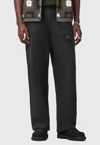 Pantaloni cargo neri con una vestibilità ampia, dotati di tasche laterali e una texture liscia. Indossati con un maglione a fantasia e scarpe nere.