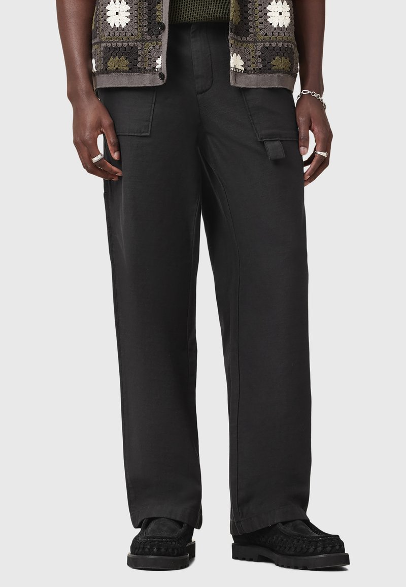 Pantaloni cargo neri con una vestibilità ampia, dotati di tasche laterali e una texture liscia. Indossati con un maglione a fantasia e scarpe nere.