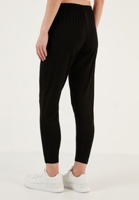 Zwarte, elastische leggings met een hoge elastische tailleband, een tapering ontwerp en een gladde textuur, gecombineerd met witte sportschoenen.
