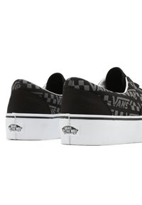 Black canvas sneakers with a checkerboard pattern, white rubber sole, and Vans logo detail on the heel. Flat, low-profile design.