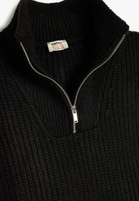 Suéter negro de punto con un alto cuello, que presenta una cremallera plateada en la parte delantera y un patrón texturizado en toda la prenda. La etiqueta dice "K&ton KIDS."