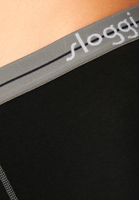 Schwarze Unterwäsche mit einem weichen grauen Gummibund, auf dem der Markenname "sloggi" in weißer Naht und einem minimalistischen Design zu sehen ist.