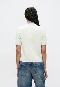 Άσπρο πλεκτό πουλόβερ με κοντά μανίκια και μπλε γιακά, συνδυασμένο με ανοιχτό μπλε ψηλόμεσο τζιν με ξεβαμμένο εφέ και πίσω τσέπες.