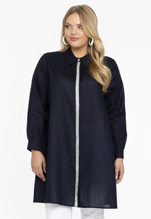 Marineblauwe lange blouse met een gekraagde halslijn, sluiting met knopen aan de voorkant en een zilveren paillettenstrip in het midden. Lichtgewicht stof.