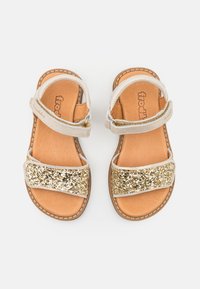 Sandales dorées scintillantes avec deux larges brides, l'une brillante et l'autre lisse, posées sur une semelle en cuir beige. Bride de cheville réglable pour un ajustement parfait.