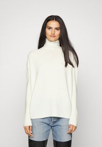 Helles Cream-Farbenes Rollkragenpullover in entspannter Passform, mit langen Ärmeln und weichem Stricktextur, kombiniert mit blauen Jeans.