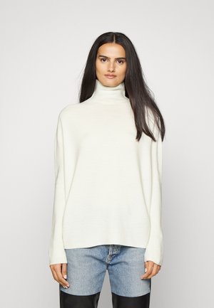 Lys kremfarget høyhalset genser i en avslappet passform, med lange ermer og myk strikket tekstur, sammen med blå denimjeans.
