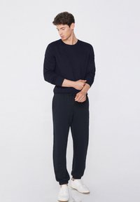 Marineblaues Langarmshirt, kombiniert mit passenden Jogginghosen, die einen Kordelzugbund und gerippte Ärmelbündchen aufweisen. Getragen mit weißen Sneakers.